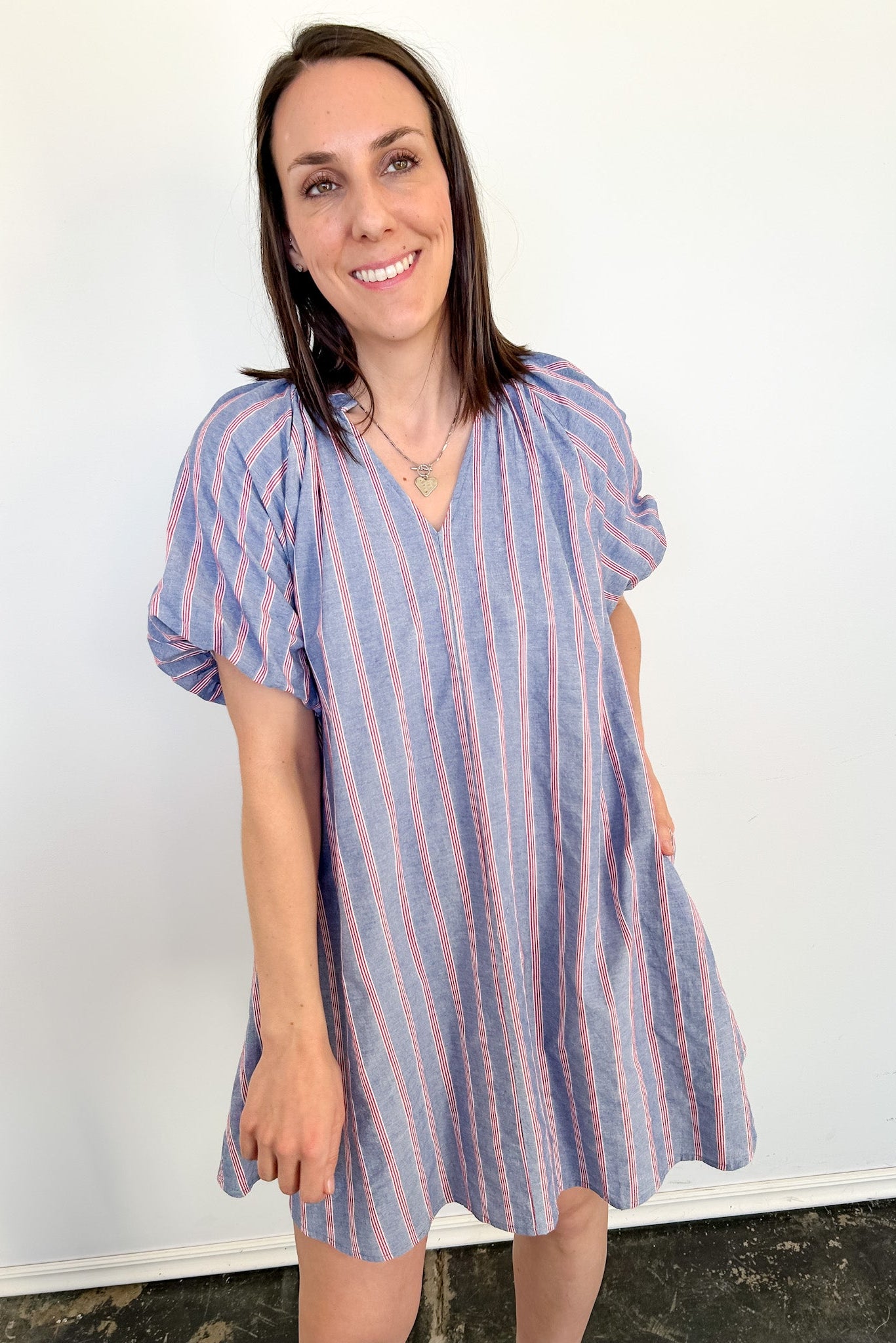 Woman wearing a blue and pink striped dress against a white wall.