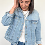 Woman wearing light wash denim jacket with white tee underneath.