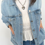 Woman wearing a light wash denim jacket with silver heart necklace.