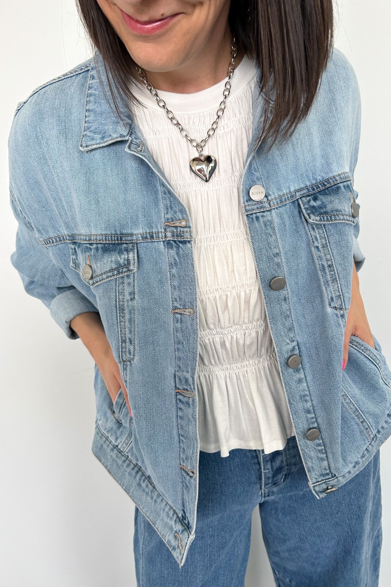 Woman wearing a light wash denim jacket with silver heart necklace.