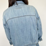 Person wearing a light blue denim jacket against a white background