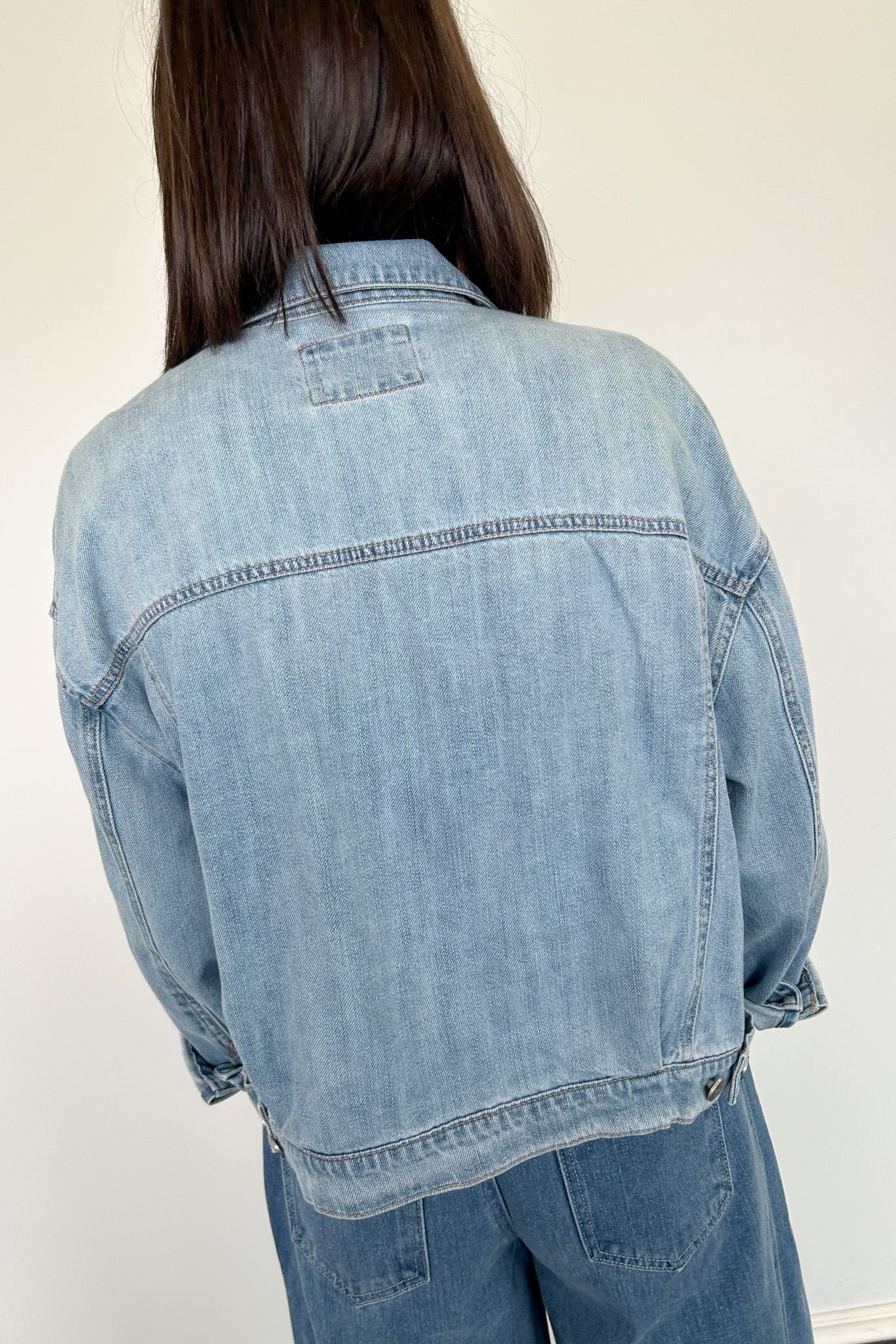 Person wearing a light blue denim jacket against a white background