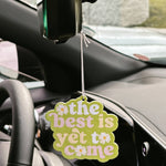 Car air freshener with 'the best is yet to come' text hanging from a car's rearview mirror.