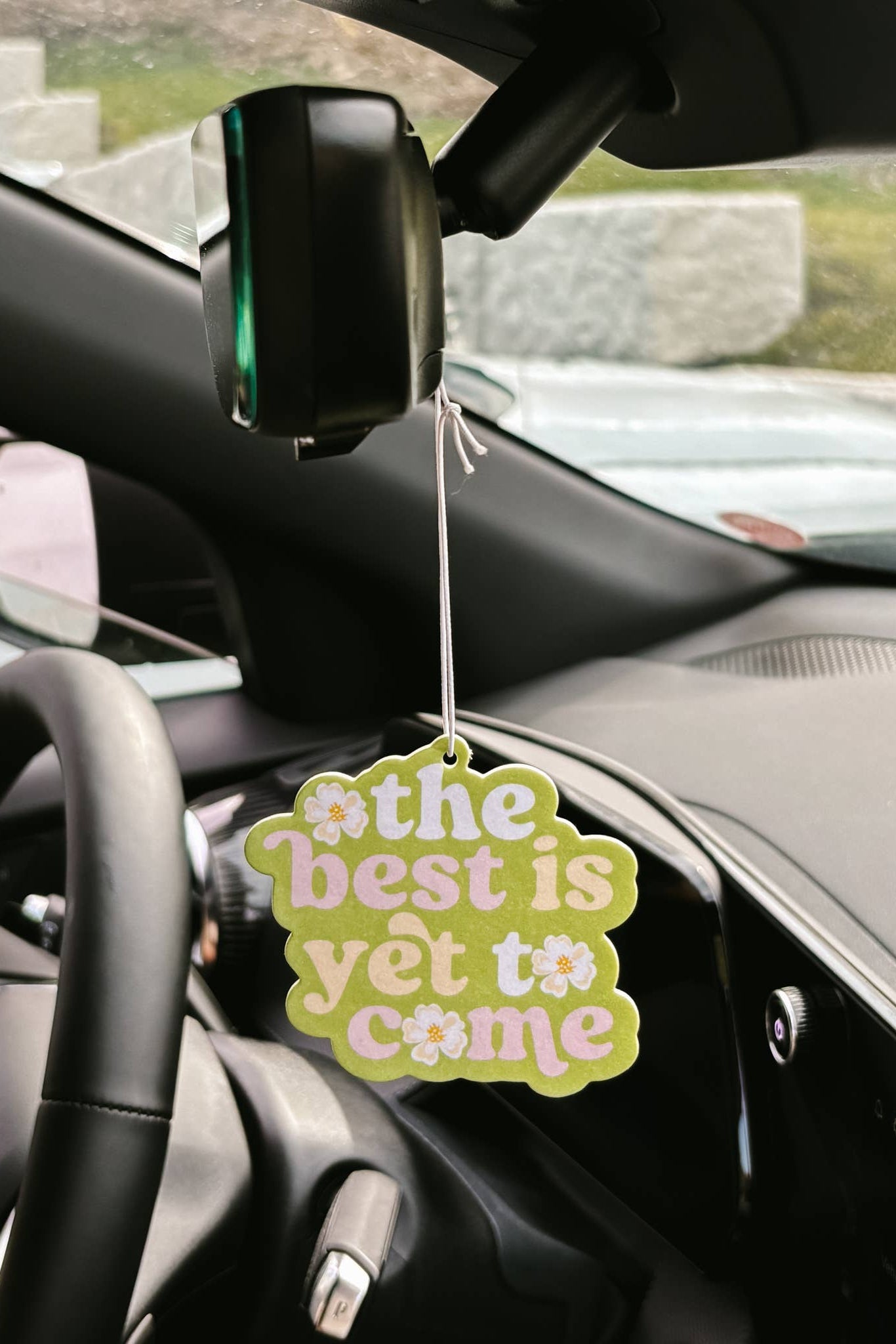 Car air freshener with 'the best is yet to come' text hanging from a car's rearview mirror.