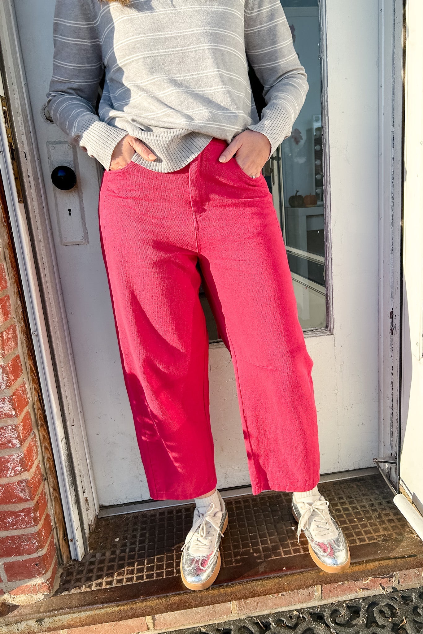Person wearing a gray sweater and pink pants standing in front of a door.