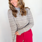 Woman wearing a gray striped sweater and red pants against a white wall
