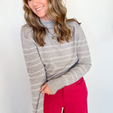 Woman wearing a gray striped sweater and red pants against a white wall
