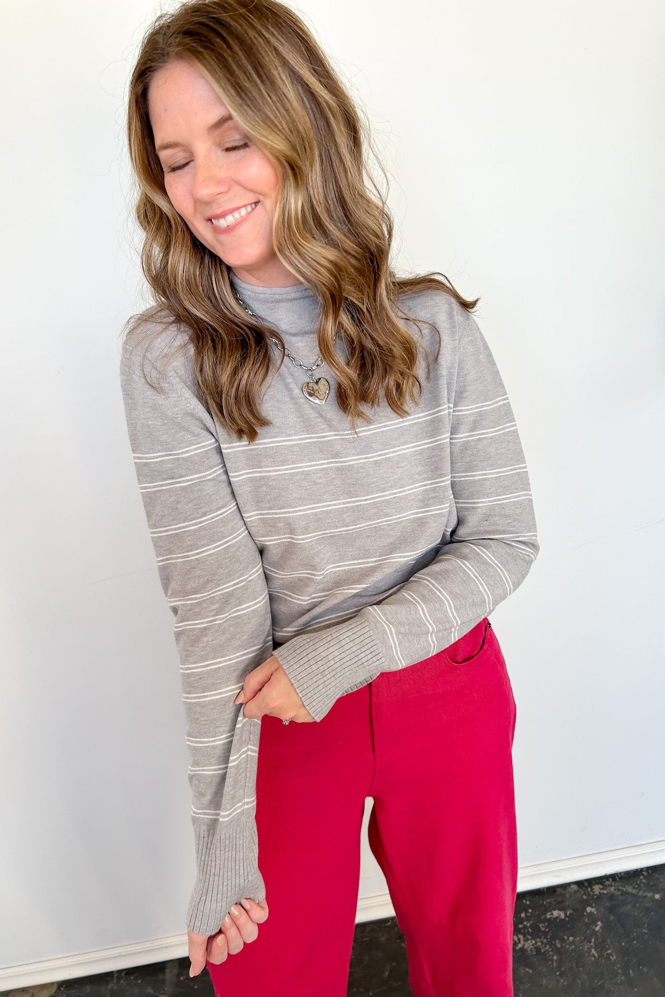 Woman wearing a gray striped sweater and red pants against a white wall