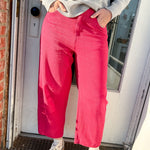 Person wearing a gray sweater and pink pants standing in front of a door.