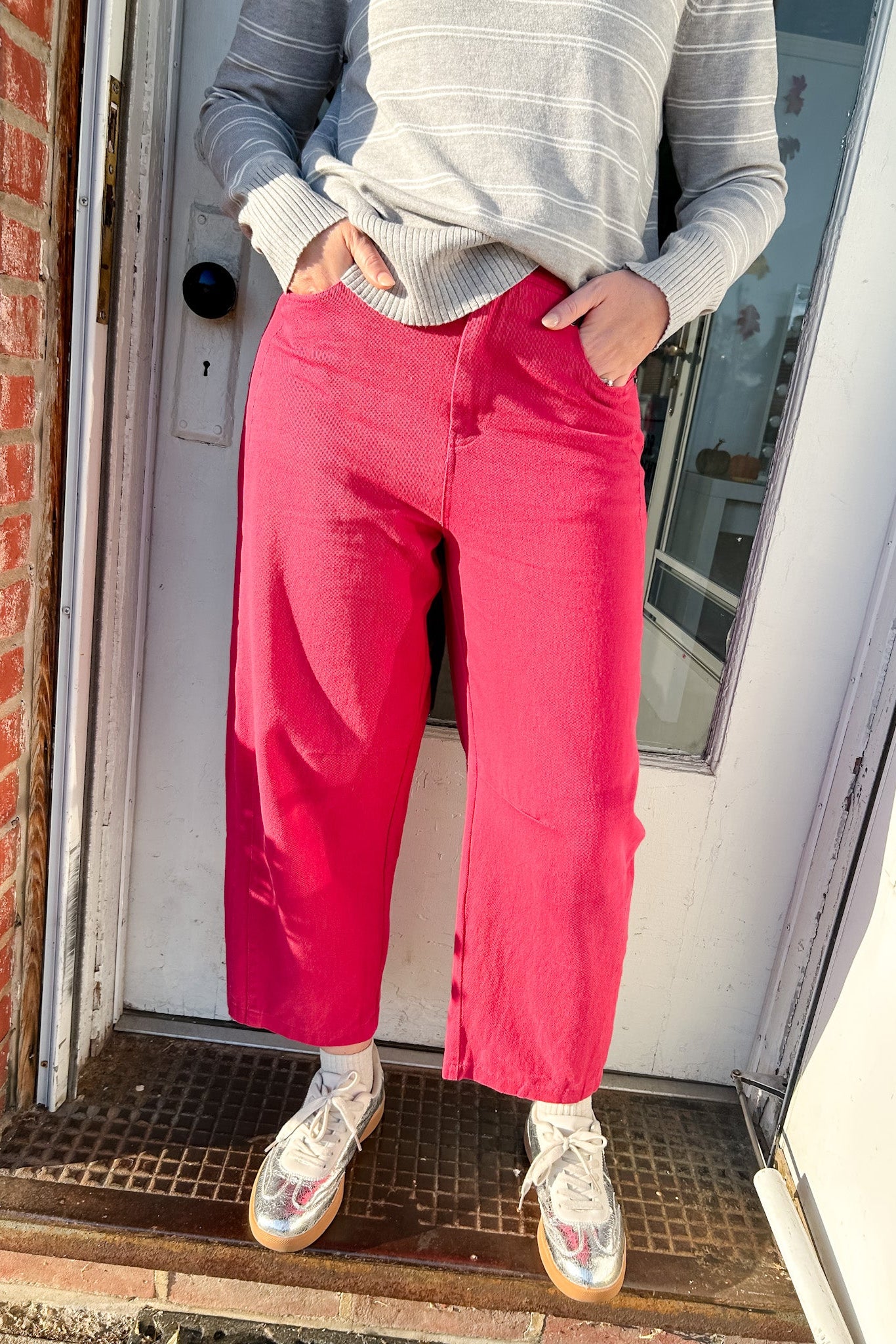 Person wearing a gray sweater and pink pants standing in front of a door.