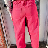 Person wearing bright pink pants standing in front of a door.