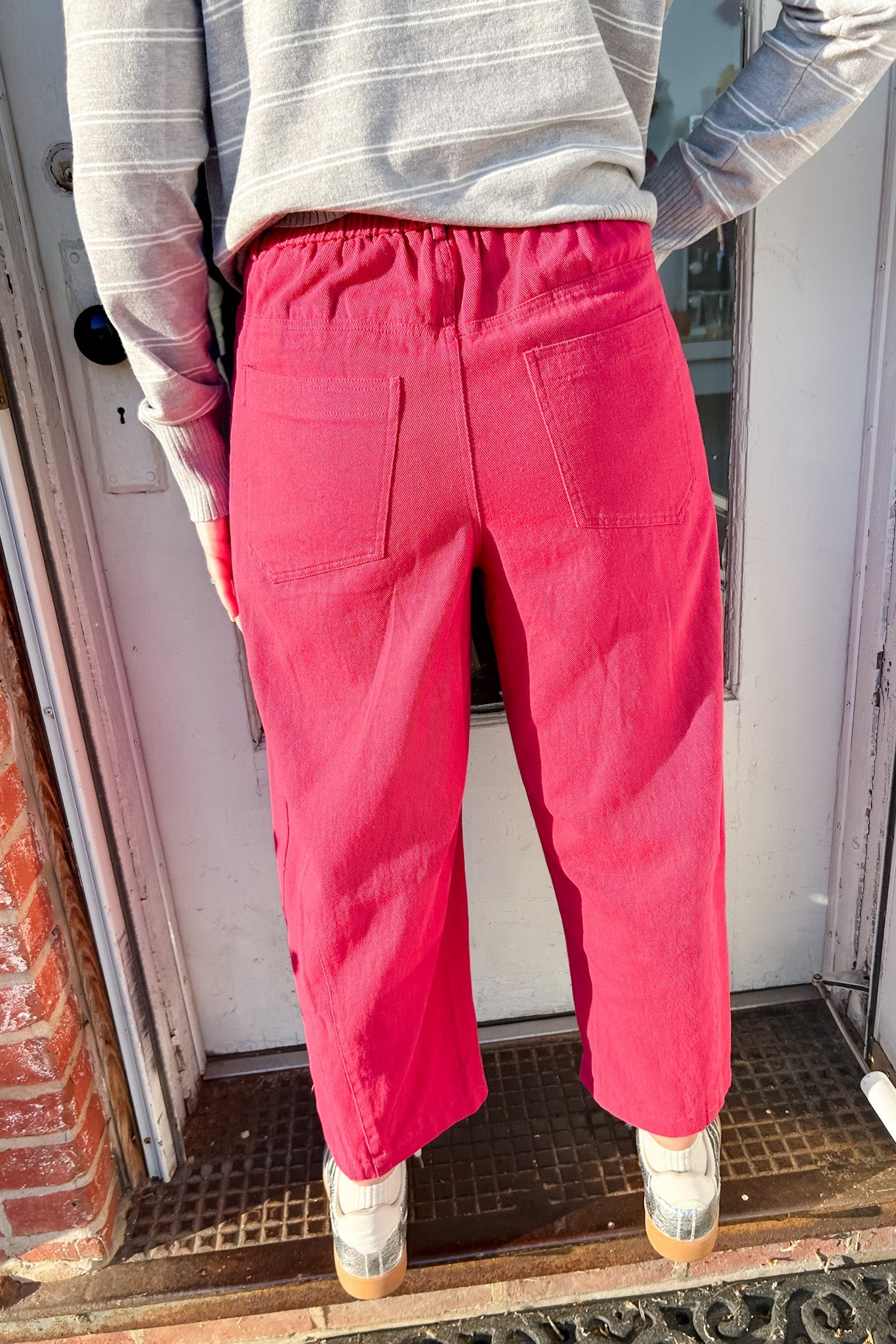 Person wearing bright pink pants standing in front of a door.