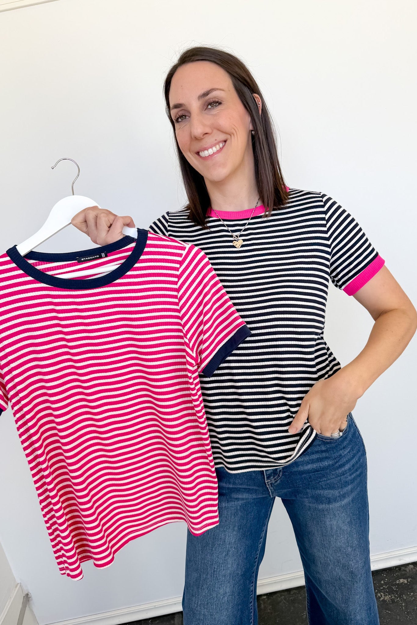 Woman holding a striped shirt and a hanger with another shirt against a white background