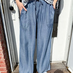 Person wearing a striped shirt and blue wide-leg pants standing on a doorstep.