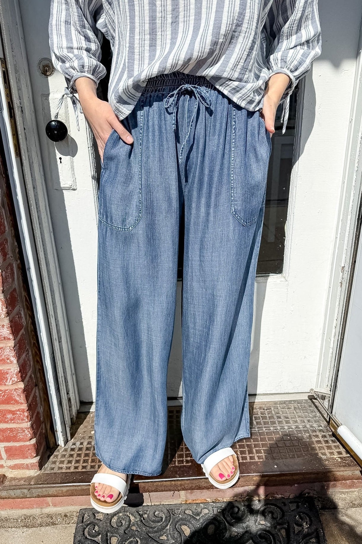 Person wearing a striped shirt and blue wide-leg pants standing on a doorstep.