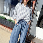 Woman in a striped shirt and wide-leg jeans standing outside a store.
