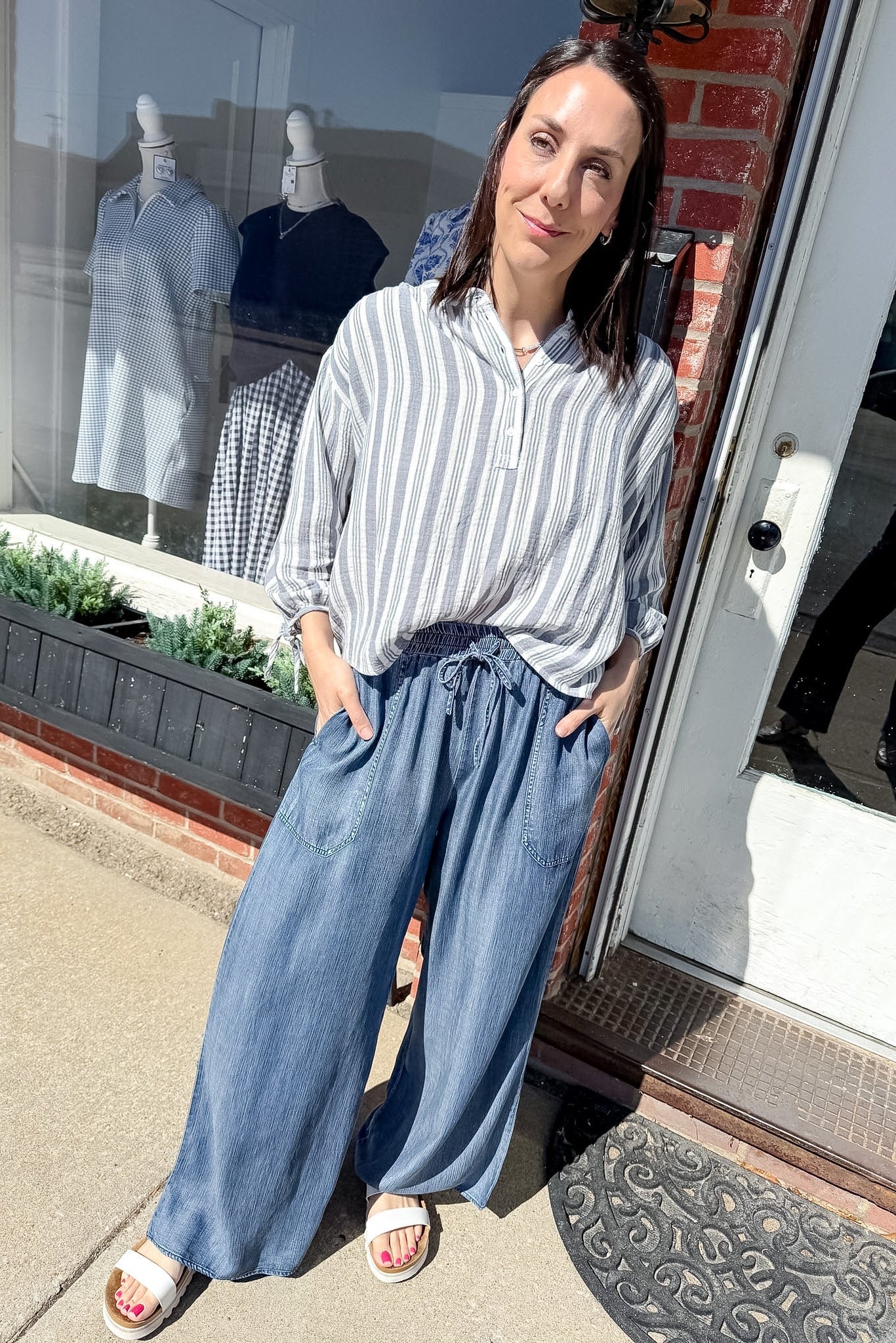 Woman in a striped shirt and wide-leg jeans standing outside a store.