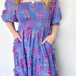 Flowy floral print dress with colors periwinkle and hot pink. Smocked bodice. Puff sleeves with tiered bottom. 