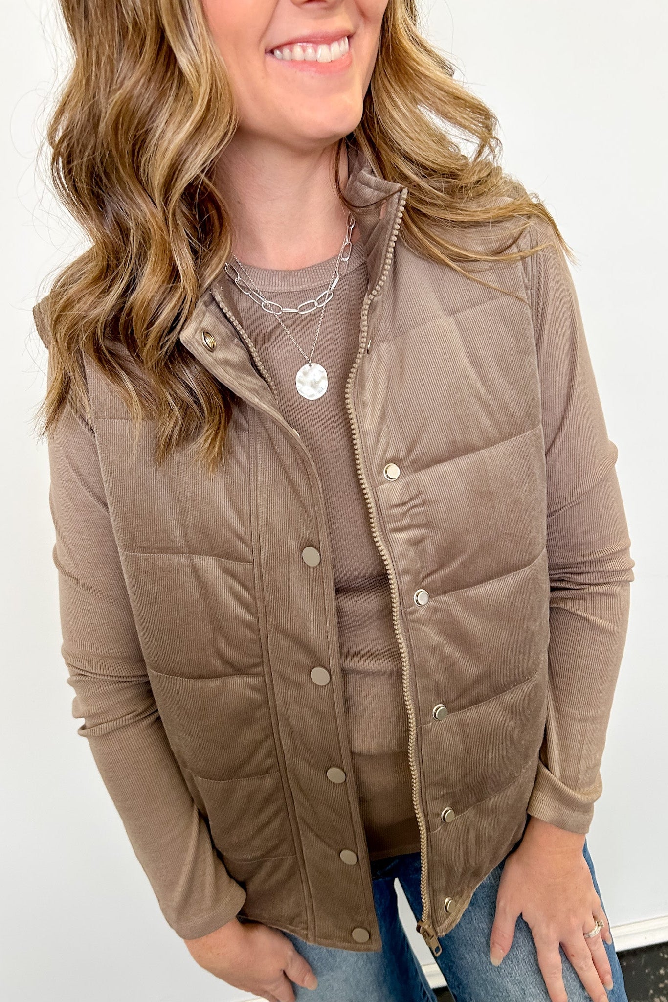 Woman wearing a brown puffer vest against a white background