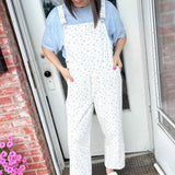 Woman wearing a light blue shirt and white patterned overalls standing on a porch.