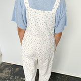 Person wearing white floral overalls and a blue shirt against a plain background