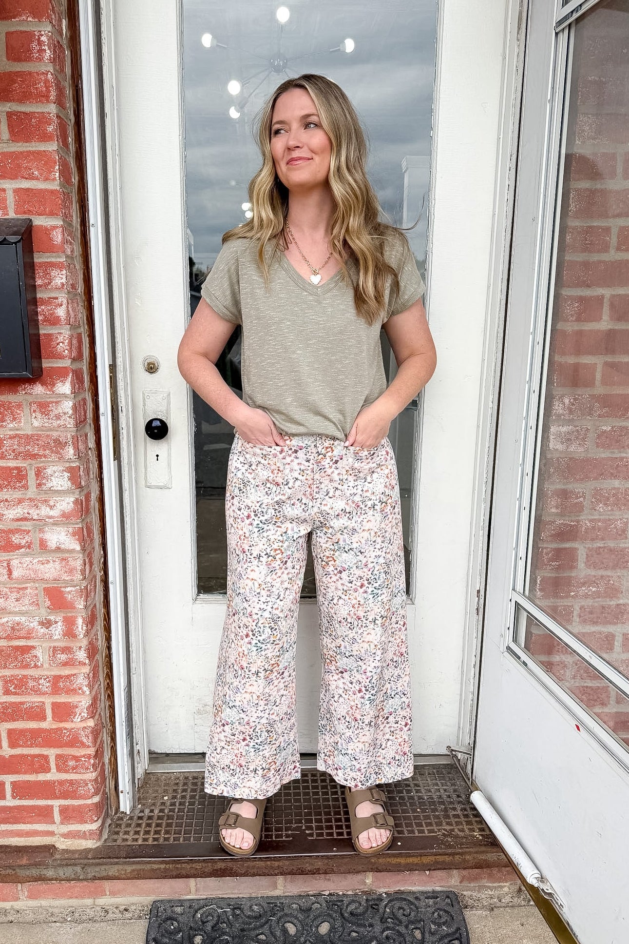 Woman standing in front of a door wearing a gray t-shirt and floral pants.