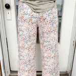 Person wearing floral pants and a green top standing in front of a door.