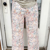 Person wearing floral pants and a green top standing in front of a door.