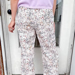 Person wearing a light purple shirt and floral pants standing on a doormat.
