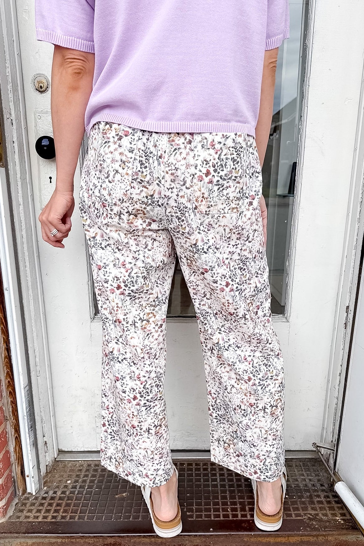 Person wearing a light purple shirt and floral pants standing on a doormat.