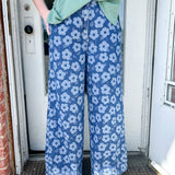 Person wearing blue floral pants and a green top standing in front of a door.