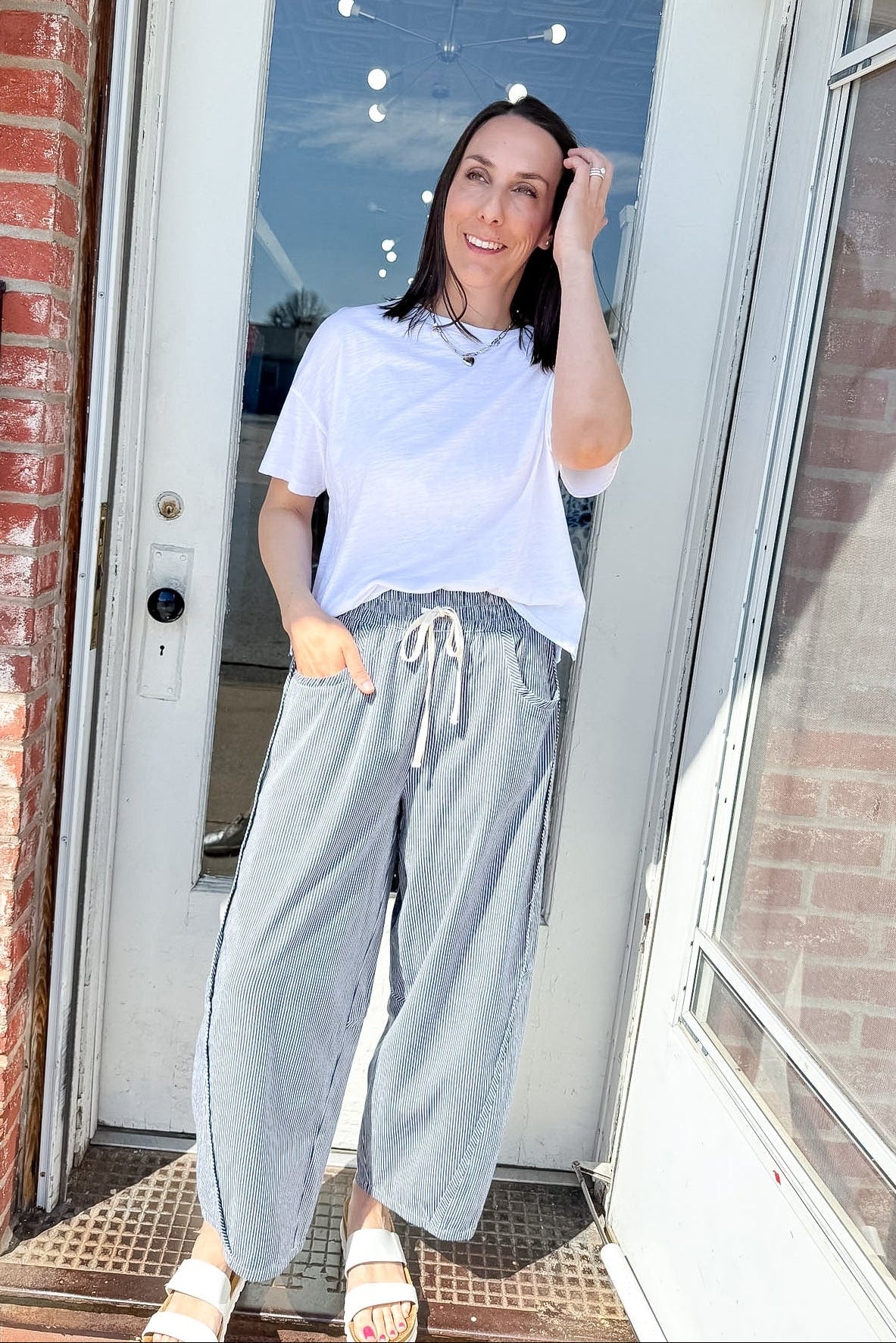 Woman standing outside a house wearing a white t-shirt and light gray sweatpants.