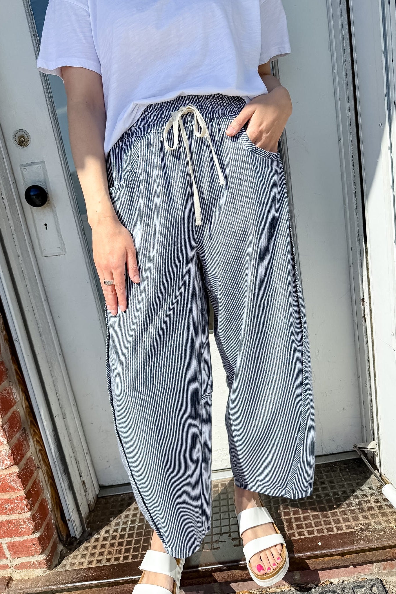 Person wearing a white t-shirt and blue checkered pants standing in front of a door.
