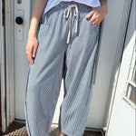 Person wearing light blue wide-leg pants and white sandals standing in front of a door.