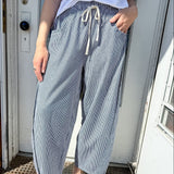 Person wearing light blue wide-leg pants and white sandals standing in front of a door.