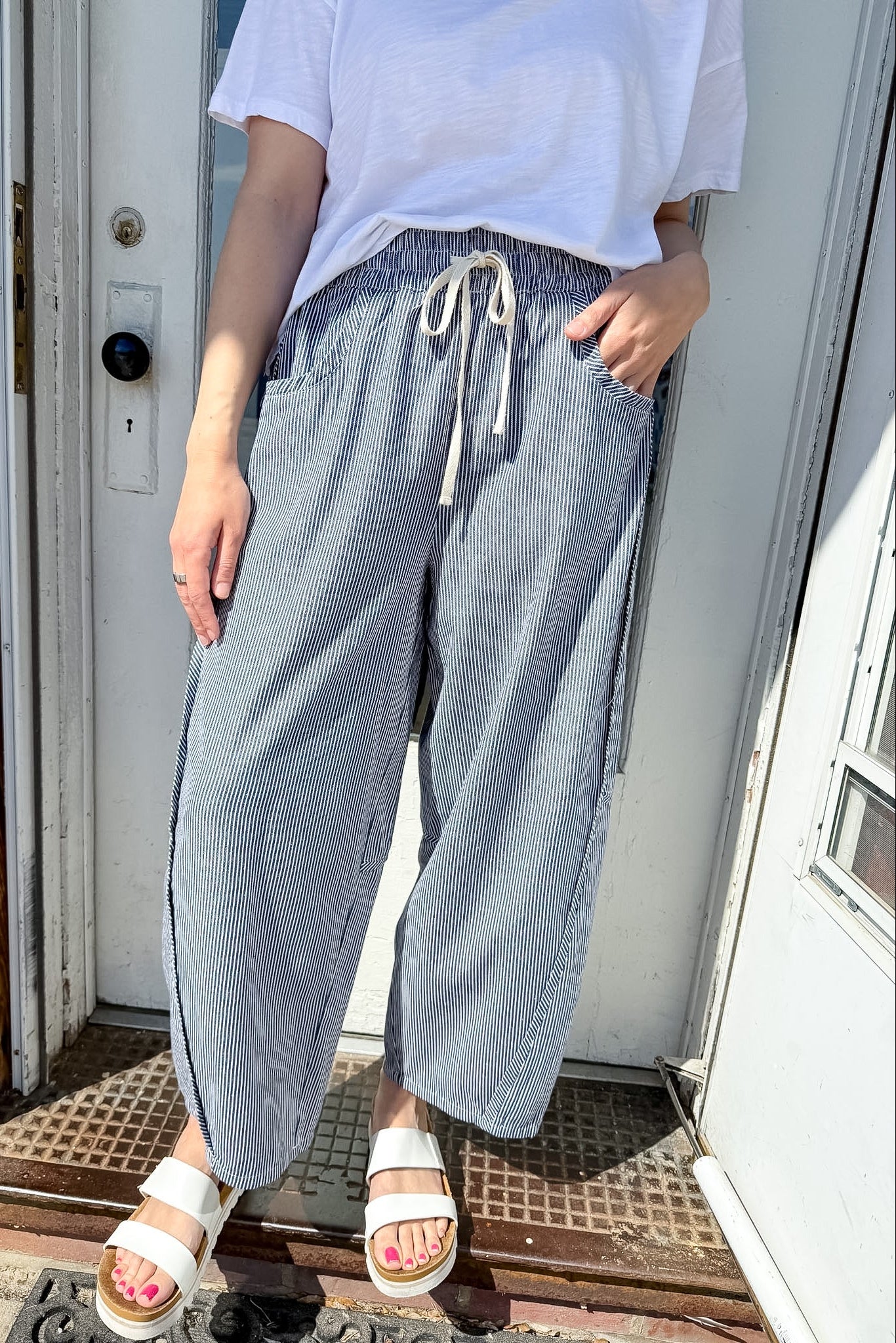 Person wearing light blue wide-leg pants and white sandals standing in front of a door.