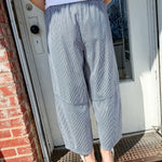 Person wearing gray checkered pants and a white shirt standing on a doormat.