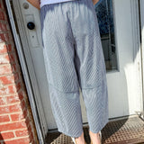 Person wearing gray checkered pants and a white shirt standing on a doormat.