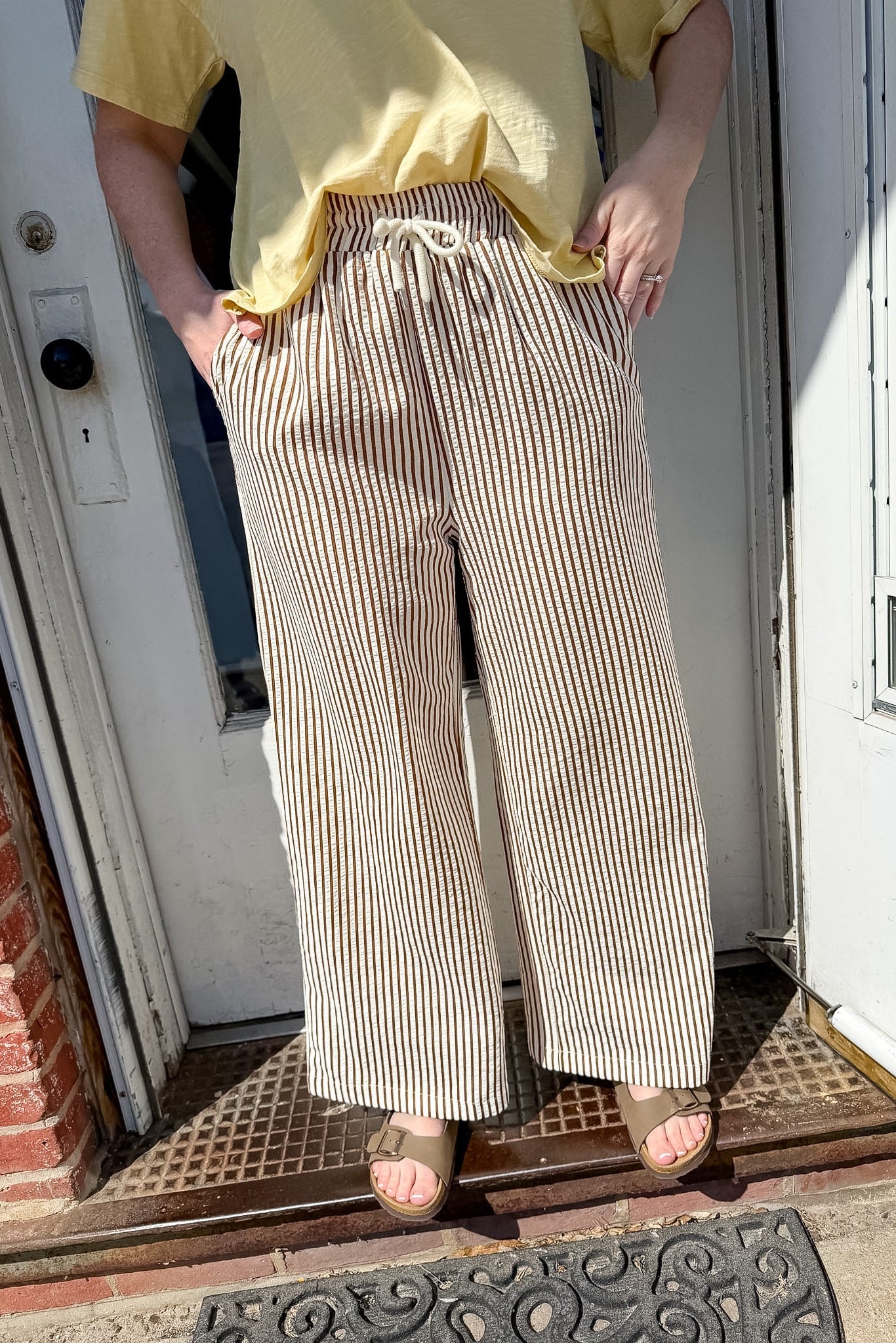 Person wearing a yellow top and striped pants standing on a doormat.