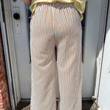 Person wearing a yellow shirt and beige striped pants standing in front of a door.
