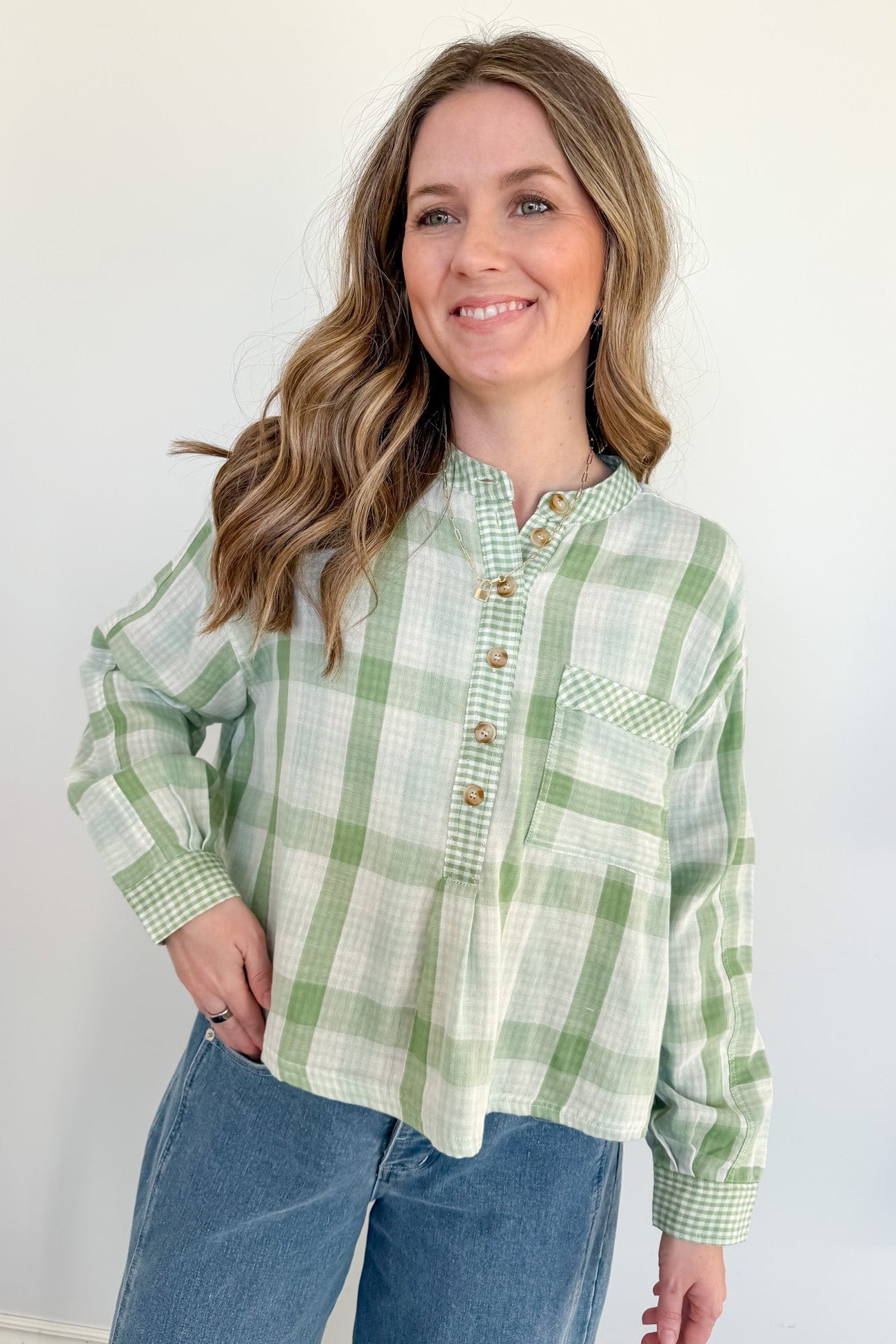 Woman wearing a green and white plaid shirt with blue jeans against a white background