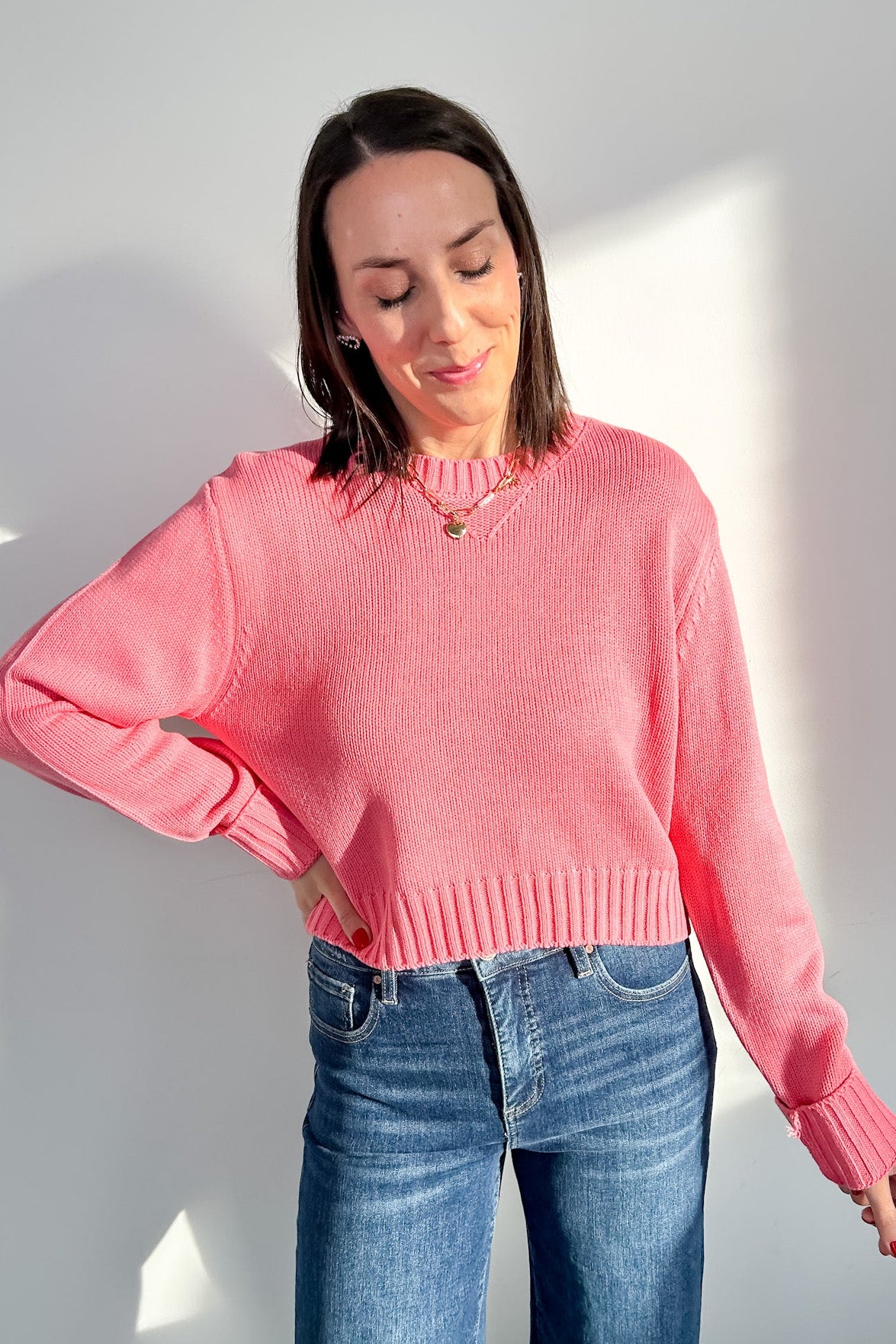 Woman wearing a pink sweater and blue jeans against a white background
