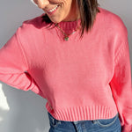 Woman wearing a pink sweater and blue jeans against a white wall
