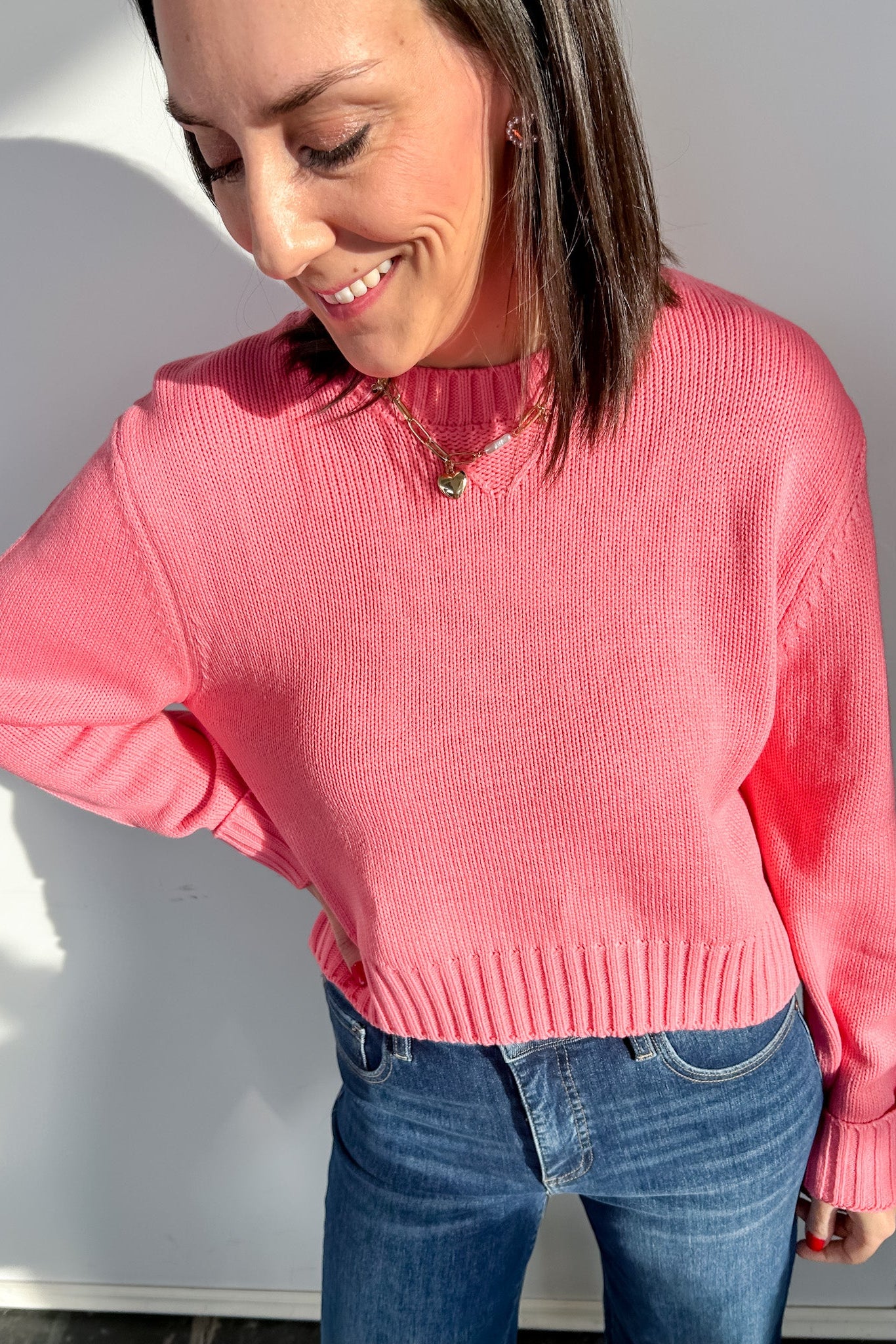Woman wearing a pink sweater and blue jeans against a white wall