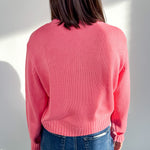 Person wearing a pink sweater and blue jeans against a white wall