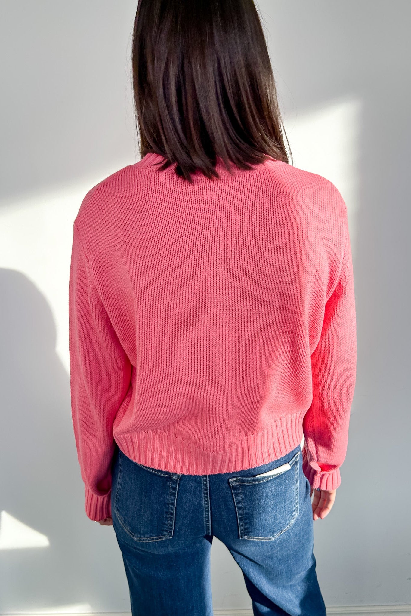Person wearing a pink sweater and blue jeans against a white wall