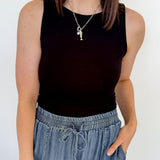 Person wearing a black sleeveless top and blue jeans against a white wall