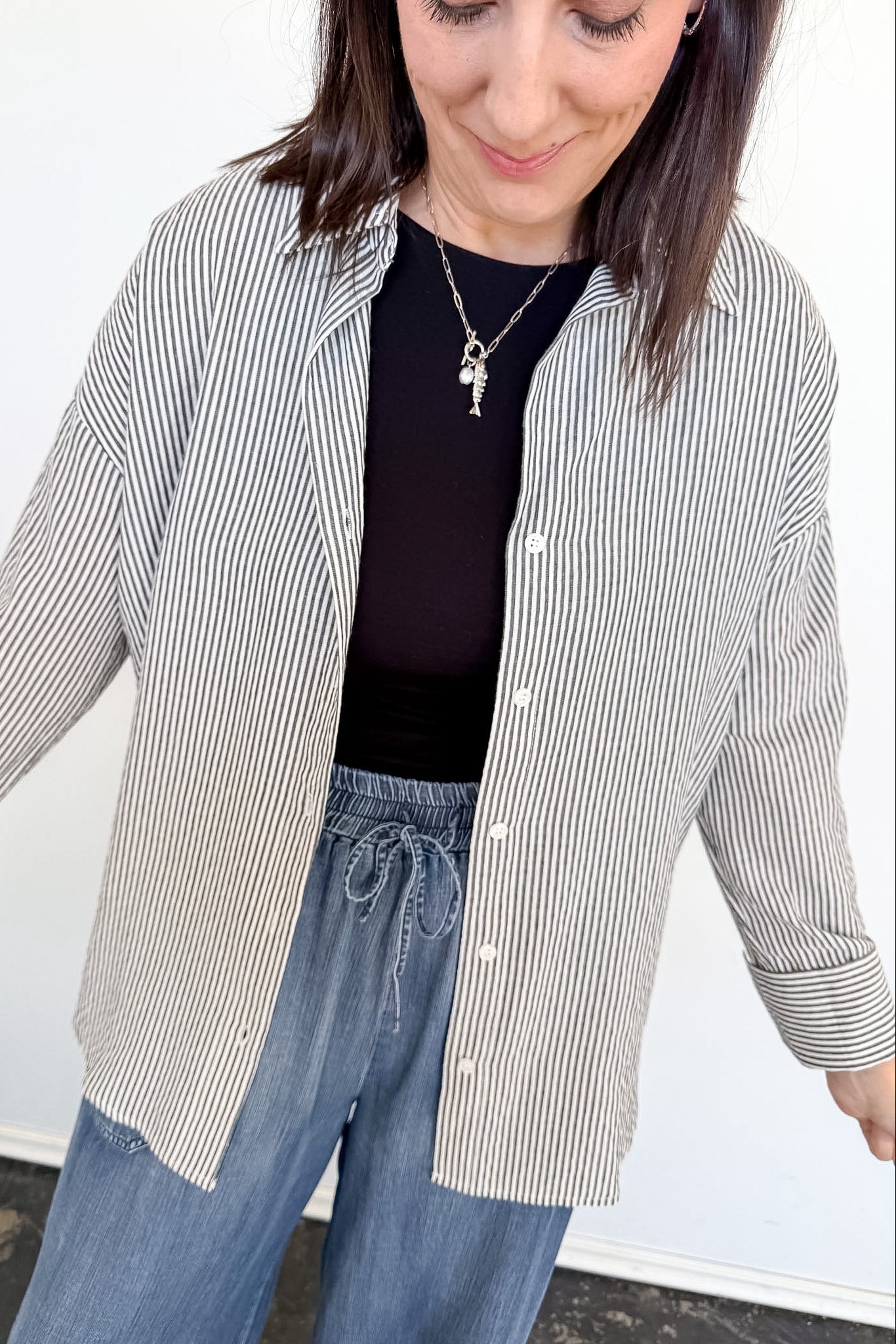 Woman wearing a striped shirt, black top, and blue jeans against a white background
