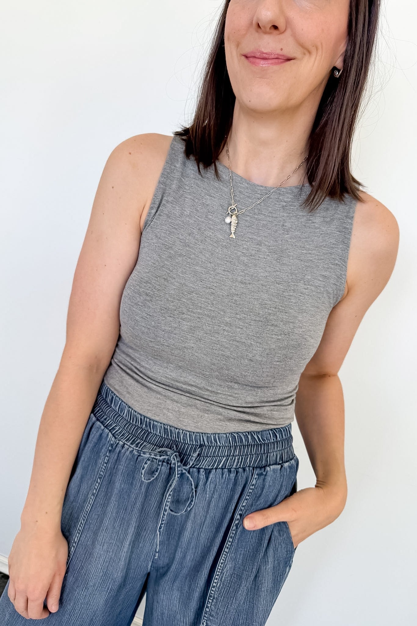 Woman wearing a gray sleeveless top and blue jeans against a white background