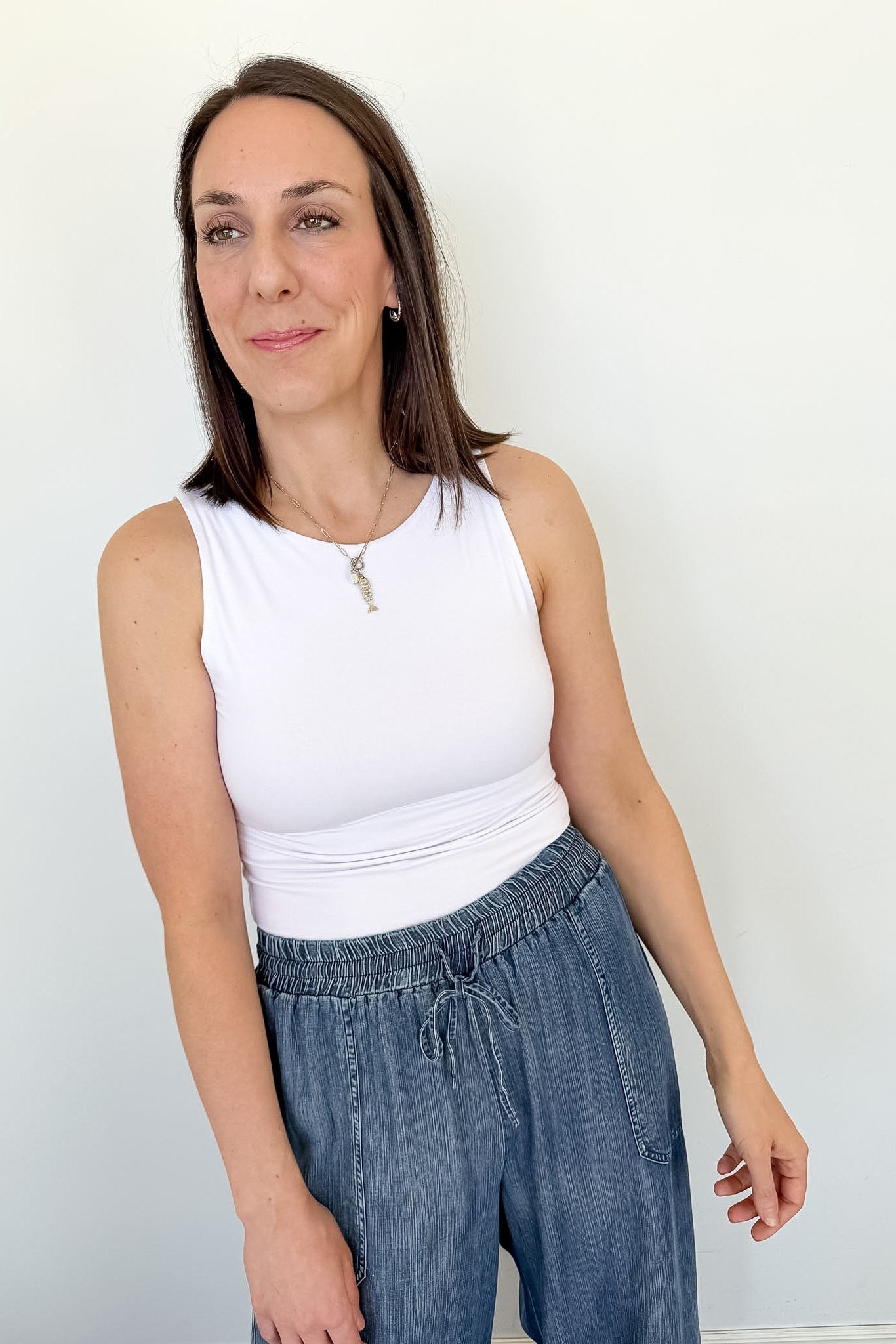 Woman wearing a white sleeveless top and blue jeans against a plain background